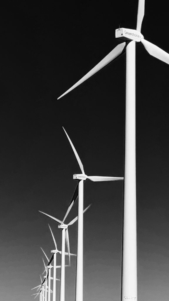 MASON JOURNAL Monochrome image of wind turbines against a clear sky, depicting renewable energy.